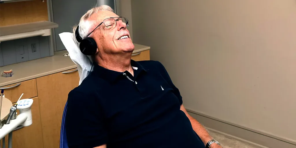 Image of a patient leaning back in a dental chair with headphones, smiling and relaxing with sedation dentistry.