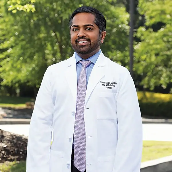 Image of Shivane Gupta, DMD, MD in a white coat, smiling.